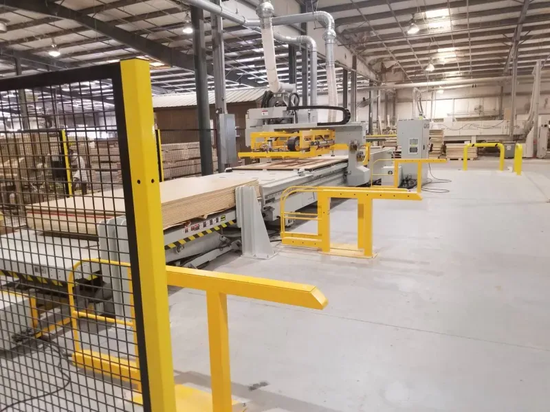 Automated CNC cell on a warehouse floor, fenced off with yellow safety rails and mesh guarding